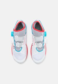 Ténis desportivos com parte superior em malha branca, accentos em vermelho e azul, e um sistema de atilhos rápido. Sola texturizada para aderência e estabilidade.