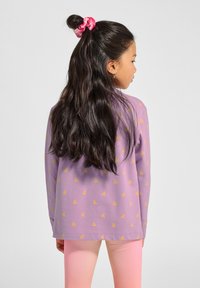 Lila Langarmshirt mit kleinen gelben Schmetterlingsmustern, getragen mit hellrosa Leggings. Haare mit einem rosa Scrunchie zusammengebunden.