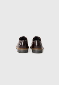 Zapatos de cuero marrón oscuro con un acabado suave, forma redondeada y una suela de goma tan en contraste, que presentan detalles de costura sutiles.