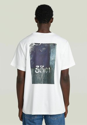 T-shirt in cotone bianco con una grande stampa grafica sul retro, che mostra una combinazione di colori blu scuro e verde con il numero "3301."