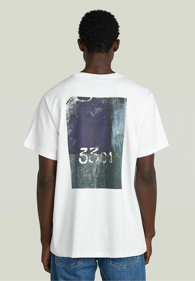 T-shirt in cotone bianco con una grande stampa grafica sul retro, che mostra una combinazione di colori blu scuro e verde con il numero "3301."