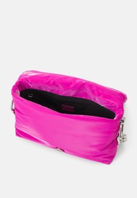 Borsa imbottita di colore rosa acceso con una texture lucida. Presenta una chiusura argentata e un interno nero con una tasca con zip. Vista aperta.