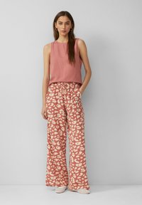 Helles pinkes �ärmelloses Oberteil, kombiniert mit lockeren, gemusterten Palazzo-Hosen mit einem cremefarbenen abstrakten Design. Einfache, lässige Schuhe runden den Look ab.