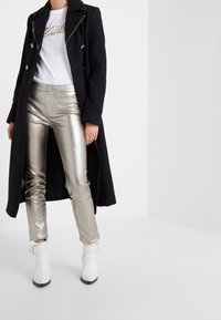 Pitkä musta takki valkoisen T-paidan päällä, yhdistettynä metallinhohtoisiin hopeisiin housuihin ja valkoisiin nilkkureihin. Takissa on kaksirivinen malli.