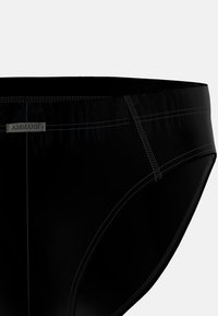 Primo piano di slip neri da uomo con cuciture visibili e un piccolo etichetta in tessuto che recita "AMMANN" sul lato della fascia.