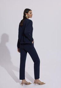 Granatowy dres wykonany z miękkiego materiału, o luźnym kroju i elastycznym pasku. Dodatki to złote kolczyki w kształcie kół oraz nude szpilki.