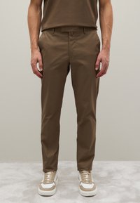 Kahki-Hosen aus einem leichten Stoff mit angepasst Passform, ausgestattet mit seitlichen Taschen und einer glatten Textur. Getragen mit beigen und weißen Sneakern.