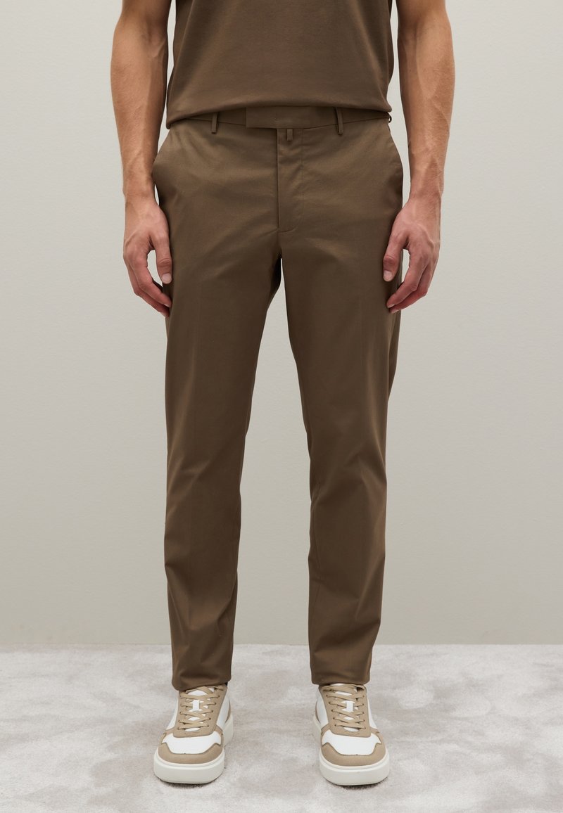 Kahki-Hosen aus einem leichten Stoff mit angepasst Passform, ausgestattet mit seitlichen Taschen und einer glatten Textur. Getragen mit beigen und weißen Sneakern.