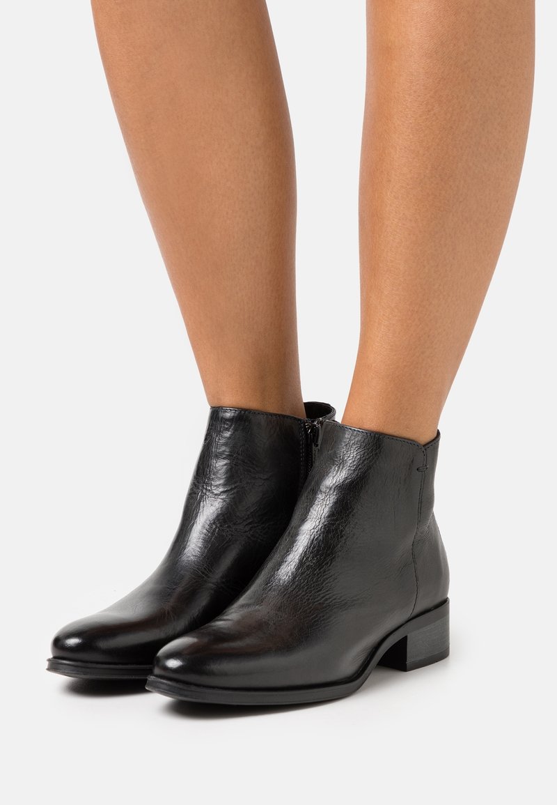 Botas de tobillo de cuero negro con textura suave, punta redonda, tacón bajo en bloque y detalles con cremallera lateral.