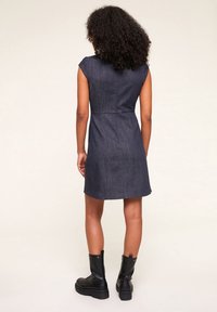 Džínové šaty s krátkými rukávy, upnutým pásem a délkou po kolena. Látka je tmavě modrá s hladkou strukturou, nošeno s černými vojenskými botami.