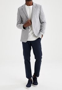 Blazer gris claro con un solo botón, bolsillo delantero, llevado sobre una camiseta blanca, combinado con pantalones azul marino y zapatos azul marino oscuro.