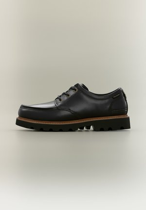 Chaussure en cuir noir à lacets avec une semelle intermédiaire épaisse marron et une semelle extérieure en caoutchouc noir robuste sur fond neutre.