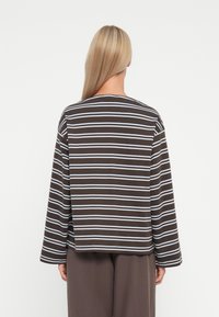 Top a maniche lunghe a righe marroni e bianche con scollatura rotonda, vestibilità comoda e texture di tessuto morbido, vista da dietro.
