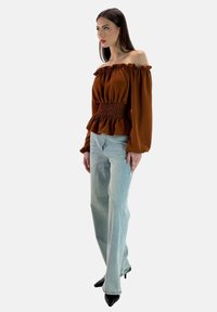 Rostfarbige schulterfreie Bluse mit gerafftem Taillenbund und Peplum-Saum, kombiniert mit hellblauen weit geschnittenen Jeans und schwarzen Stilettos.