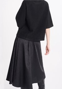 Maglione cropped nero in tessuto testurizzato abbinato a una gonna nera fluida, caratterizzata da un motivo sottile e una finitura liscia.