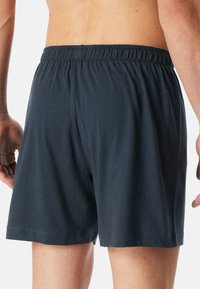 Pantaloni corti neri in cotone con elastico in vita, caratterizzati da un design semplice e una texture liscia. L'orlo termina appena sopra le ginocchia.