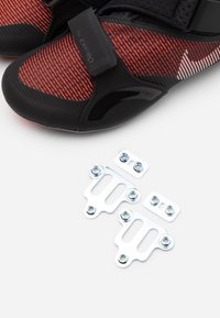 Buty treningowe Nike SuperRep mają czarno-czerwony design z teksturowaną cholewką i gładką podeszwą. Dołączone są srebrne metalowe zaczepy na kolce.