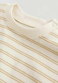 Chemise pour bébé couleur crème avec des rayures horizontales beiges, col rond et fermeture à boutons-pression sur l'épaule pour un habillage facile.