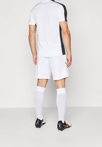 Vit sporttröja med svarta detaljer, kombinerad med vita shorts och knälånga vita strumpor. Har en texturerad meshdesign. Svarta fotbollsskor.