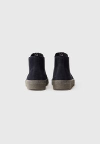 Bottines en daim noir avec une semelle grise texturée, dotées d'une languette et d'un design simple. Tige lisse avec un bout arrondi.