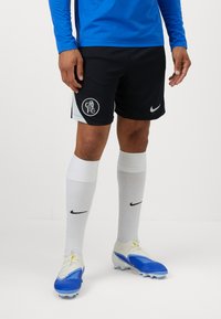 Sorte Nike-shorts med en klubblogo, parret med hvide sokker med et sort swoosh og blå fodboldstøvler med hvide detaljer.