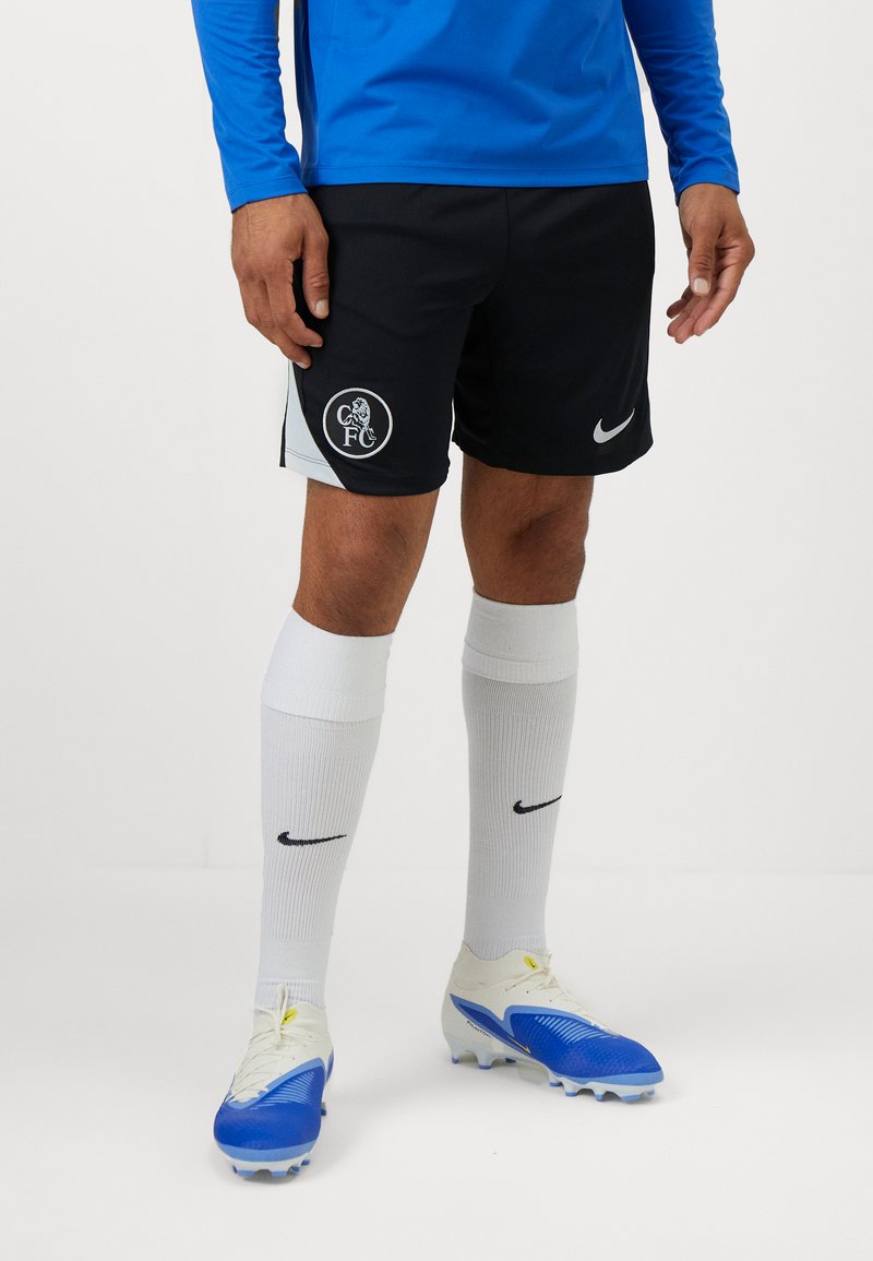 Sorte Nike-shorts med en klubblogo, parret med hvide sokker med et sort swoosh og blå fodboldstøvler med hvide detaljer.