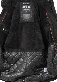 Sort fleece-foret jakke med en quiltet sort inderside, synlig mærkeetiket og en lomme til hovedtelefoner på ærmet.