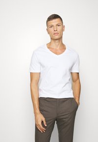 Hvid bomulds T-shirt med V-udskæring og korte ærmer, parret med brune strukturerede ternede bukser. Glat tekstur, tætsiddende design.