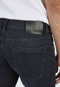 Ciemnoniebieskie dżinsy wykonane z denimu, z czarną skórzaną naszywką na pasku z logo, tylnymi kieszeniami z dokładnym przeszyciem.