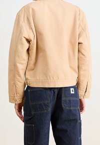 Giacca beige chiaro con vestibilità comoda, orlo curvo e bottoni a pressione, abbinata a pantaloni cargo blu scuro con tasche frontali.