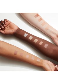 Campioni di trucco su tre braccia di diverse tonalità di pelle. I campioni mostrano sfumature varie: crema, beige chiaro, taupe e bronzo.