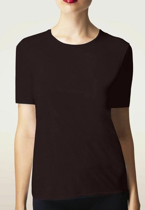 Vrouw draagt een effen zwart T-shirt met korte mouwen, rode lippenstift, getoond van schouders tot heupen tegen een lichte achtergrond.