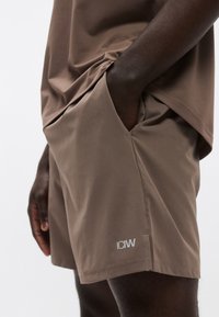 Καφέ αθλητικές σορτς με λεία υφή, πλαϊνές τσέπες και μικρό λευκό λογότυπο "ICIW" στο τελείωμα. Ελαφρύ και αναπνέον υλικό.