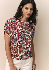  haut à manches courtes avec un motif floral et paisley coloré et complexe dans les tons rouge, bleu, vert et blanc. Tissu léger à texture côtelée.