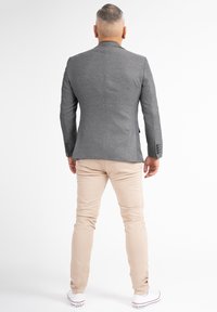 Blazer grigio strutturato con un design aderente, abbinato a chinos beige e sneakers bianche. Il blazer presenta una fessura singola e polsini con bottoni.