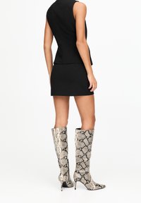 Bottes mi-mollet à bout pointu en imprimé serpent avec une finition brillante. Caractérisées par une silhouette ajustée et un talon aiguille pour allonger la silhouette.