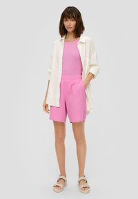 Roze tanktop, roze textuur short met zakken, en een witte oversized overhemd met knopen. Beige gevlochten sandalen maken de outfit af.