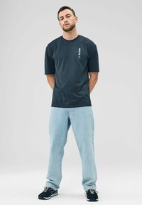 Navy t-shirt with short sleeves, round neckline, and white text graphic on the front. Paired with light blue loose-fit jeans and black sneakers.
