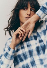 Pull en tricot avec un motif tie-dye bleu et blanc, présentant un col rond et des poignets côtelés, une texture douce et une coupe décontractée.