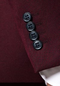 Bordowa tkanina o fakturze z czterema czarnymi guzikami przy mankiecie. Guziki mają cztery otwory i tłoczone logo dla dodatkowego efektu.