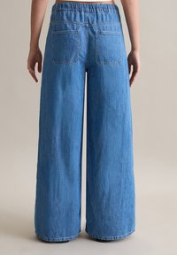 Pantalons en denim à jambes larges de couleur bleu clair, présentant un tissu texturé, une taille élastique et deux poches arrière.