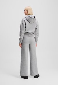 Šedá mikina s kapucí a volným střihem v kombinaci s kalhotami s širokými nohavicemi ve stejném odstínu. Měkká tkanina, minimalistický design, žádné viditelné vzory.