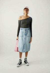Top cinza de um ombro só, saia midi de denim azul clara com dois bolsos frontais, bolsa rosa, sapatilhas pretas de cano alto e meias brancas até ao tornozelo.