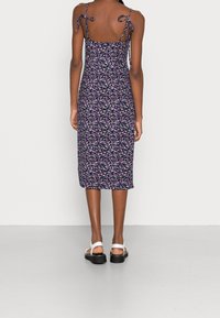 Kvetinové midi šaty se spaghetti ramínky a detaily na zavazování. Námořnický základ s vícebarevným květinovým vzorem. Měkká látka s přiléhavým střihem.