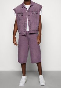Lila Denim-Weste mit Kragen-Design und zwei Taschen, kombiniert mit lila Denim-Shorts. Ein weißes T-Shirt und weiße Sneakers vervollständigen das Outfit.