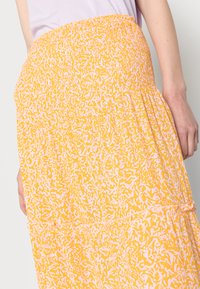 Saia amarela com cintura franzida, com um padrão abstrato branco. O tecido é leve, com um design fluido e em camadas.