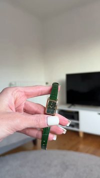 Rectangular watch with a gold-tone case, green crocodile-patterned leather strap, dark green face, white markers, and a small date display.