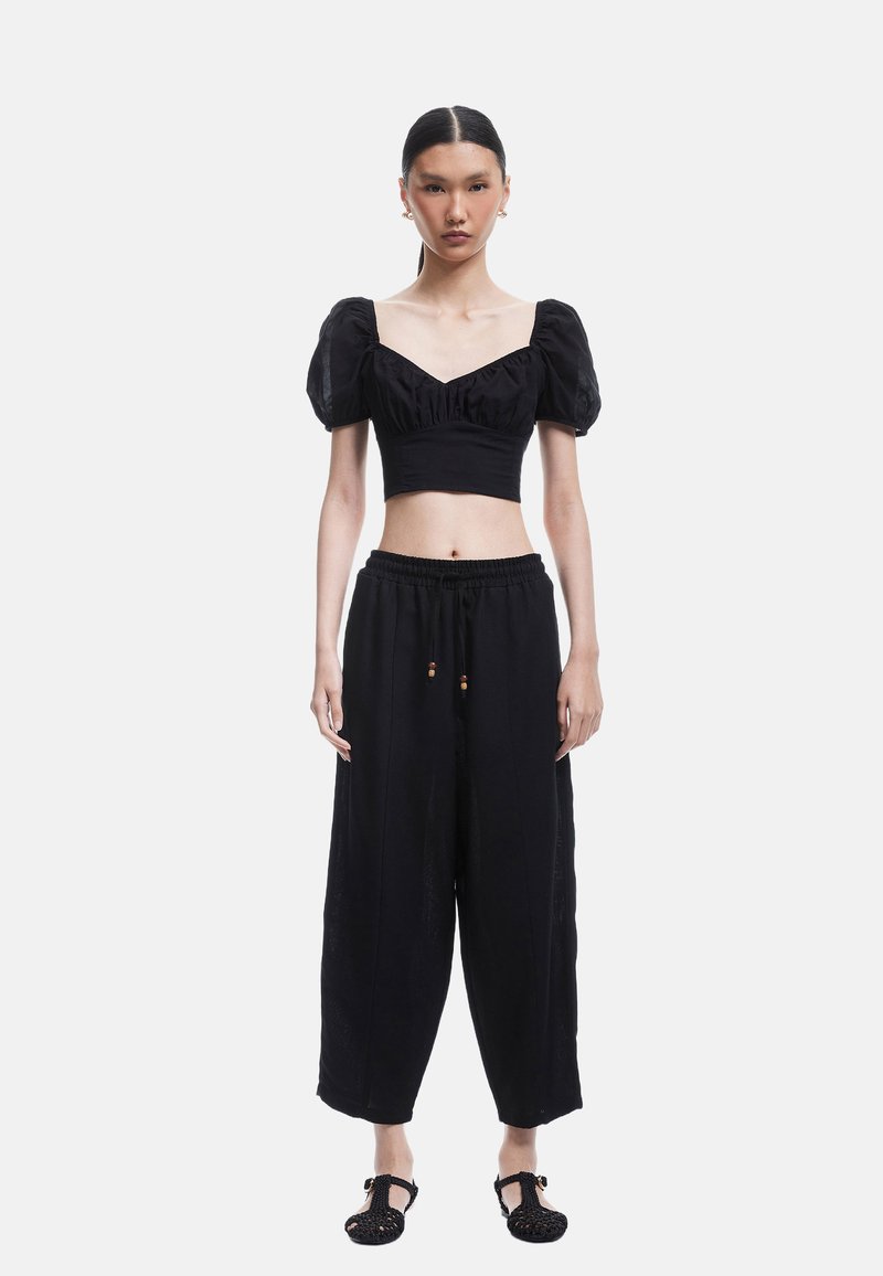 Sort cropped top med puffærmer og V-hals. Kombineret med løse sorte bukser med snor. Sorte teksturerede sko fuldender outfittet.