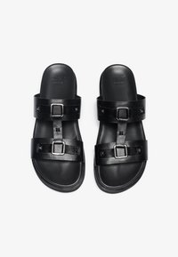 Zwarte leren sandalen met twee banden, voorzien van rechthoekige gespen en kleine driehoekige accenten. Soepele textuur en open ontwerp.