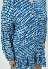 Blaues Kleid mit einem Blattmuster, vollem Saum und langen Ärmeln. Hergestellt aus weichem Stoff mit einem lockeren Schnitt und V-Ausschnitt.